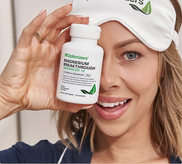 Smiling woman holding BIOptimizers Magnesium Breakthrough, wearing a sleep mask